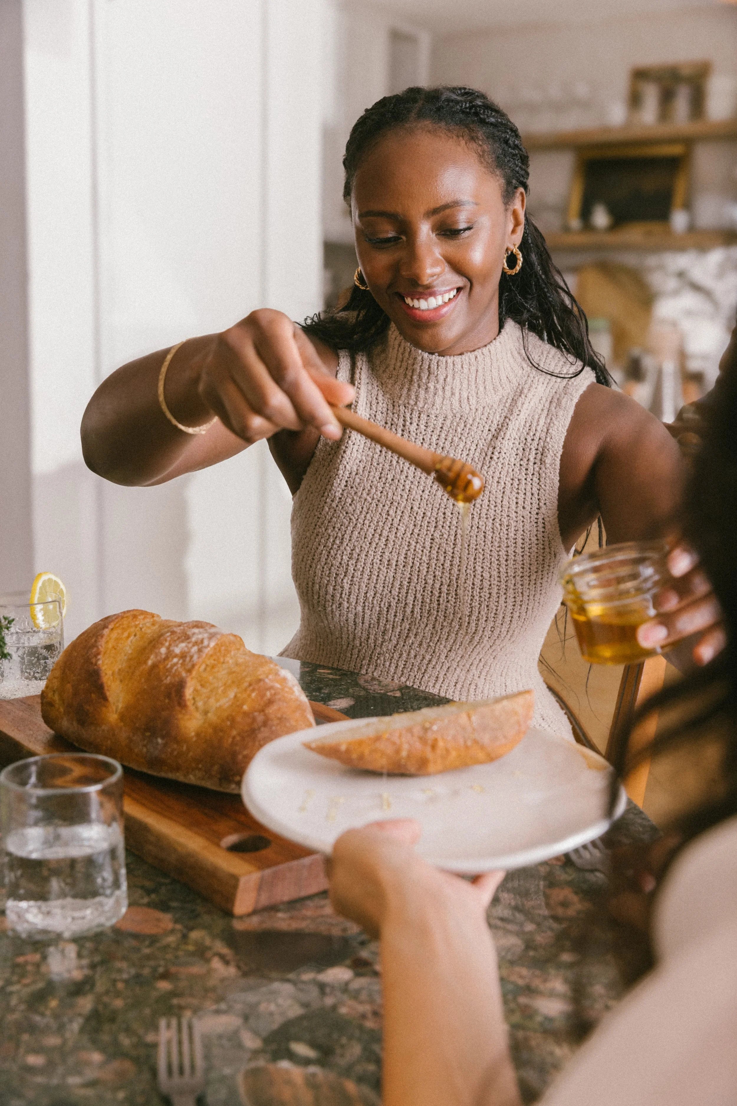 Beautiful Black woman drizzling honey onto bread, showcasing Oshun’s use of nourishing, natural ingredients like manuka honey in luxury skincare.