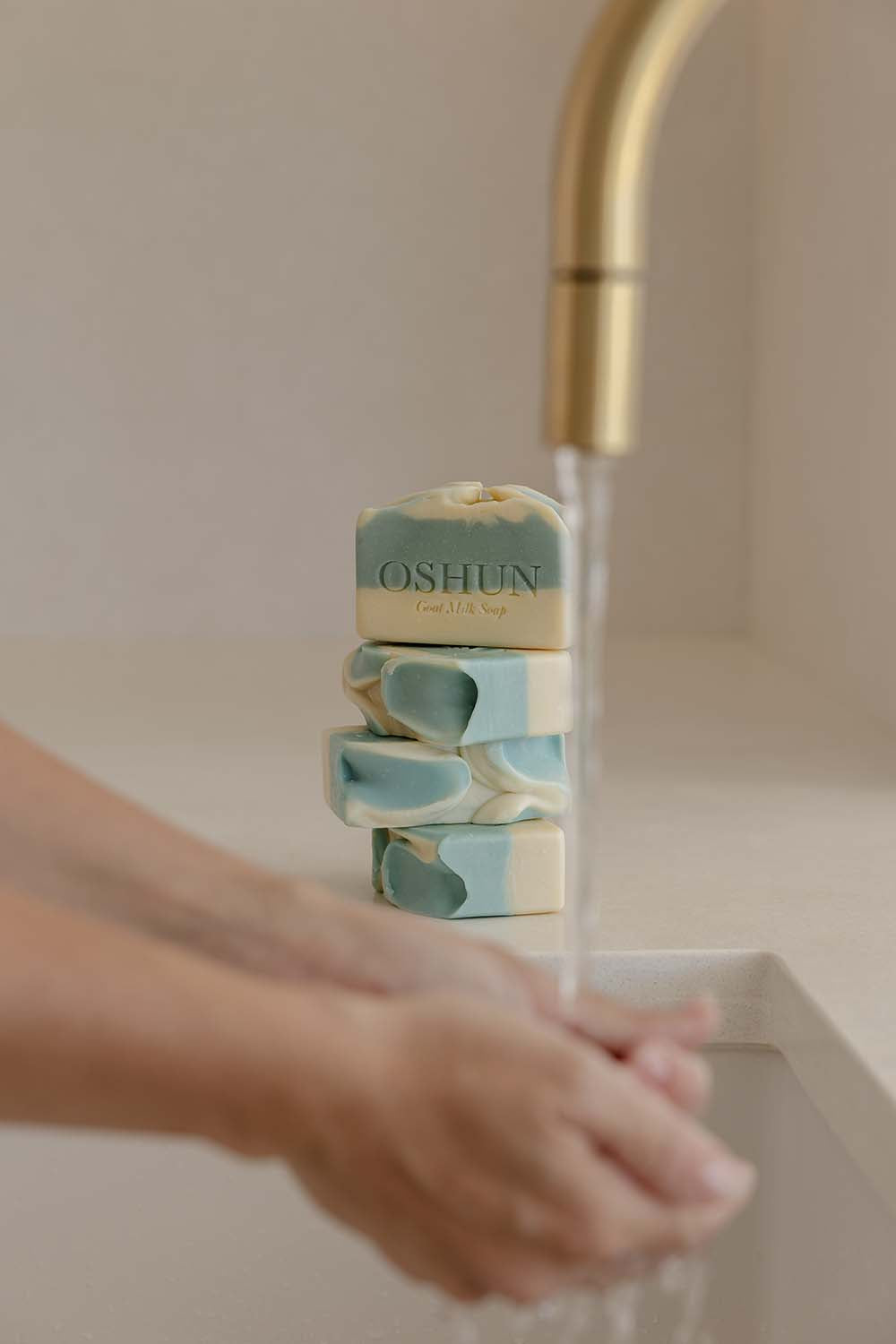 Stack of Oshun soap bars on a sink with running water