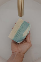 Hand holding a bar of soap with 'OSHUN' branding.