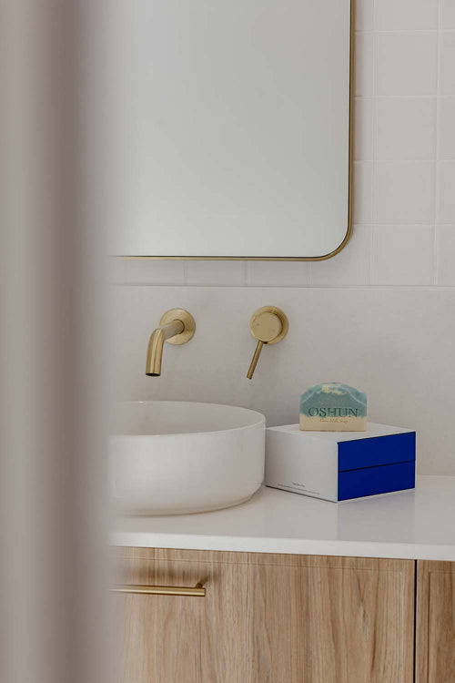 Bathroom vanity with white sink, gold faucet, and an Oshun soap bar on packaging.