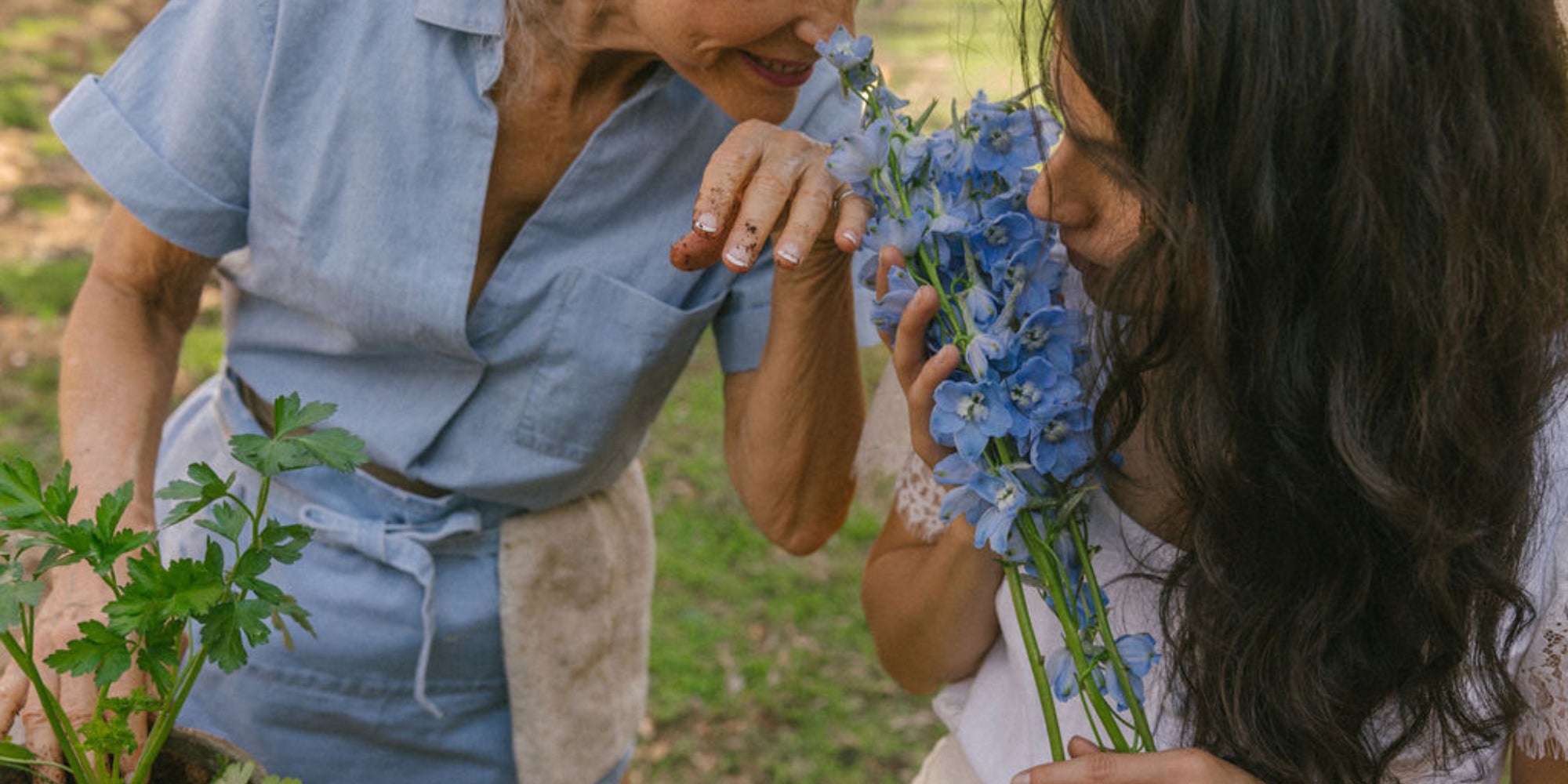 Older woman and younger woman smelling flowers in a garden, representing timeless beauty and luxury clean skincare with Oshun goat milk soap.