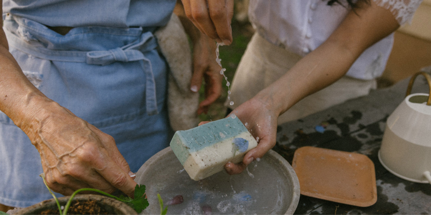 Older woman and younger woman washing hands outdoors with Oshun goat milk soap—natural, fragrance-free luxury skincare.