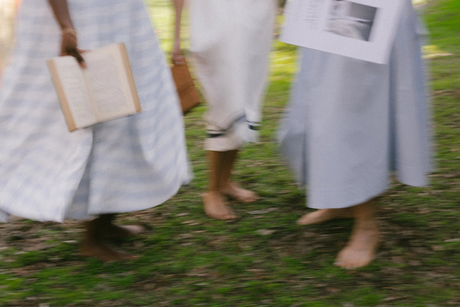 Three diverse women standing in a sunlit field, holding a journal and a book, embodying Oshun Society’s ritual, connection, and clean beauty lifestyle.